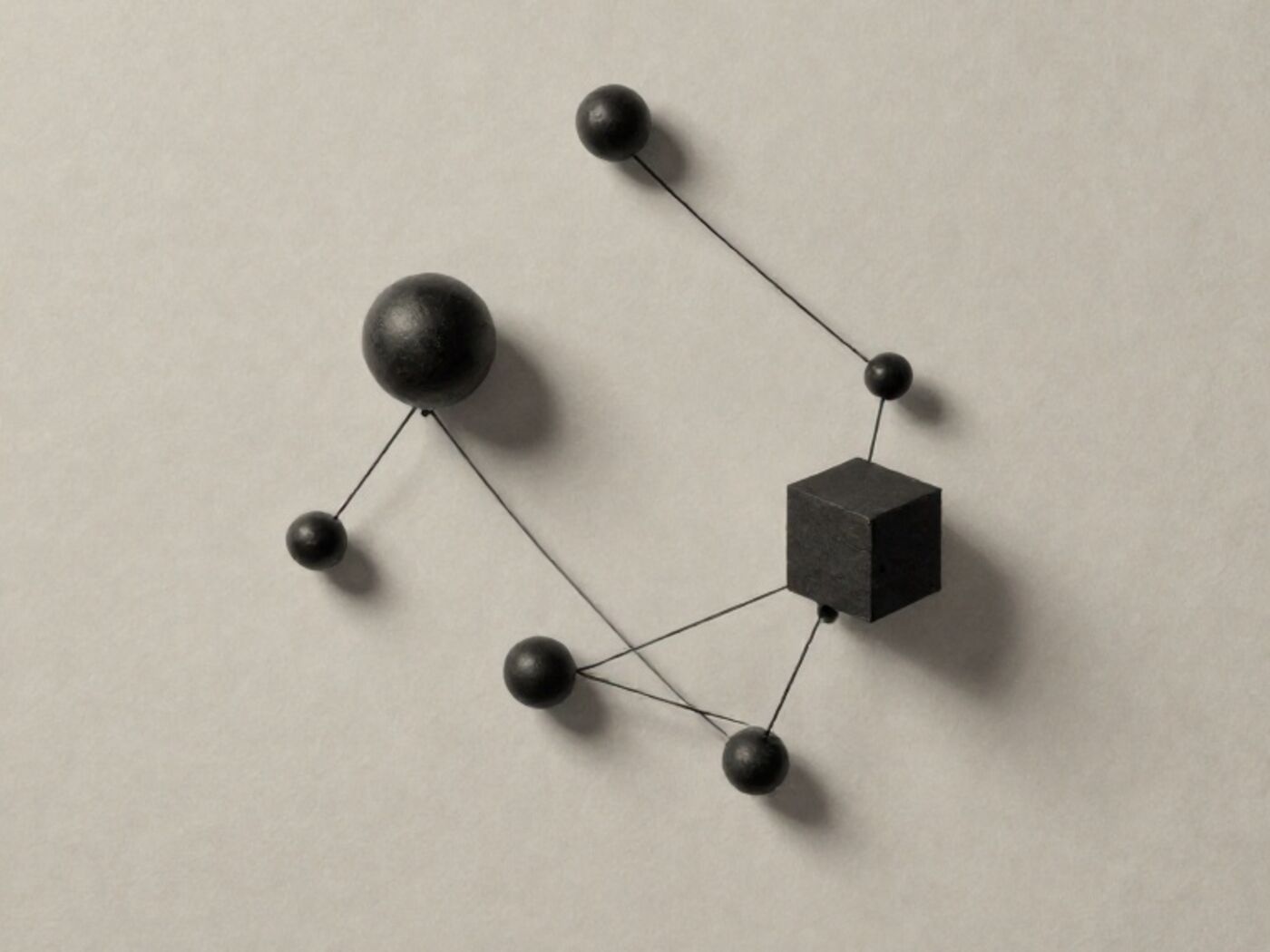 Small spheres and one cube arranged in a constellation and joined by taut black thread